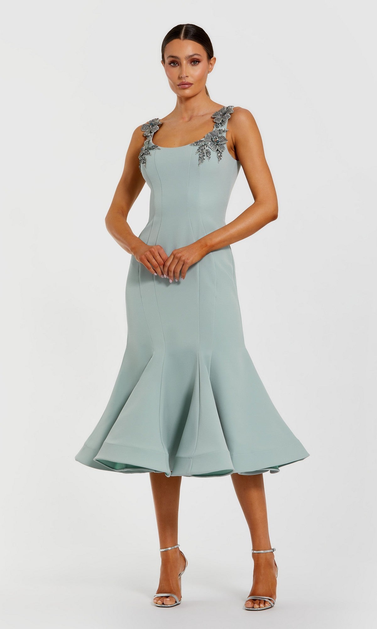A woman in a seafoam Mac Duggal 11948 midi wedding guest dress with 3D floral-embellished shoulders and sleeveless fit-and-flare silhouette, wearing heels against a plain white background.